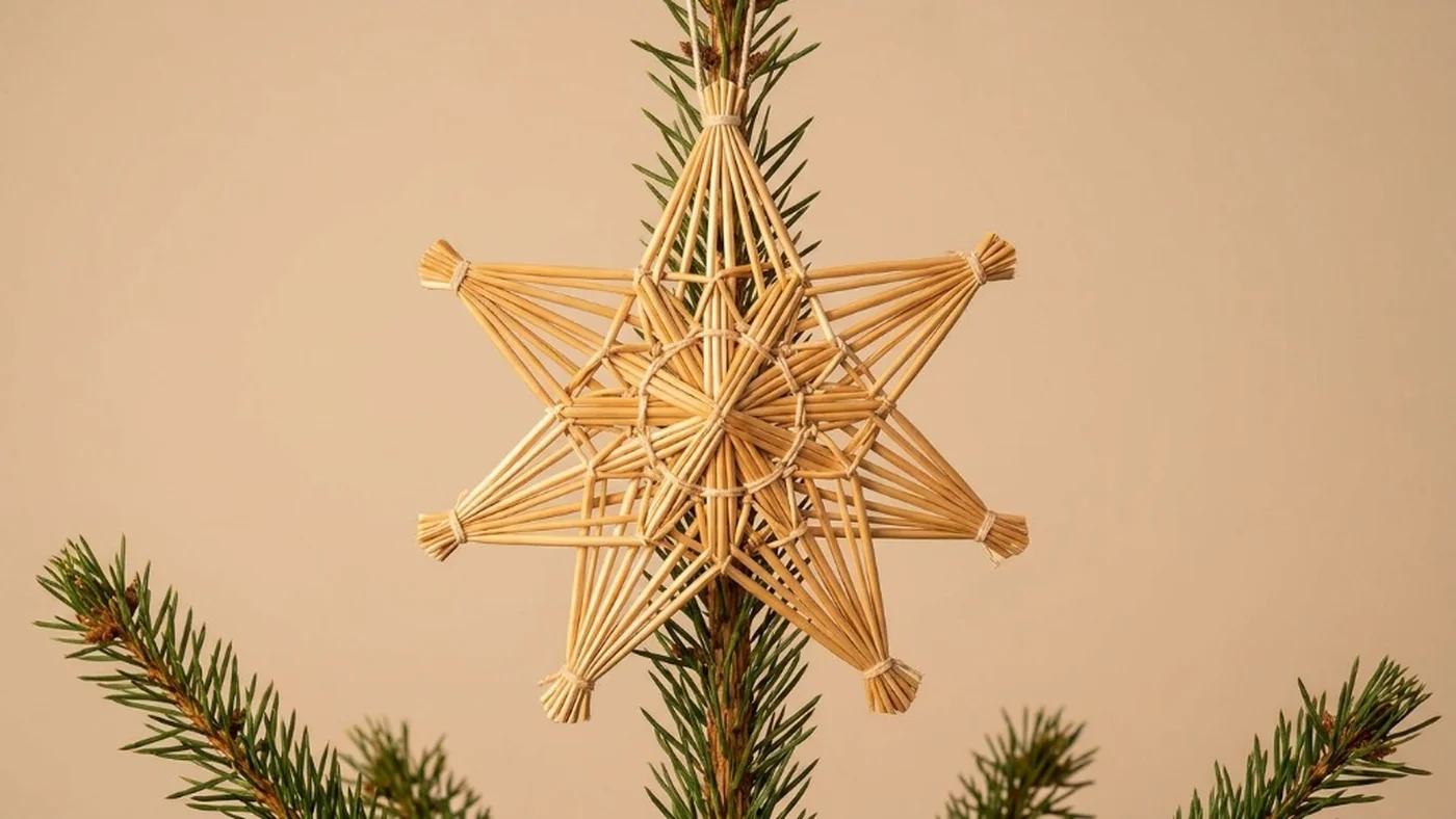 Hand-woven geometric natural straw star topper mounted firmly on the top pine branch of an evergreen Christmas tree