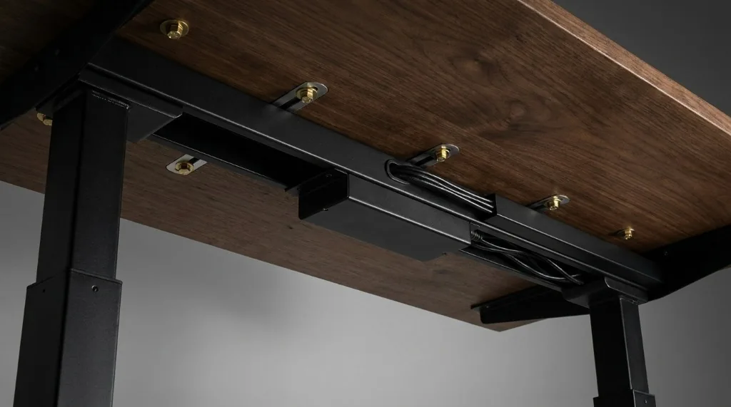 Underside view of an electric standing desk showing dual motor housing, steel crossbeams, and integrated cable management